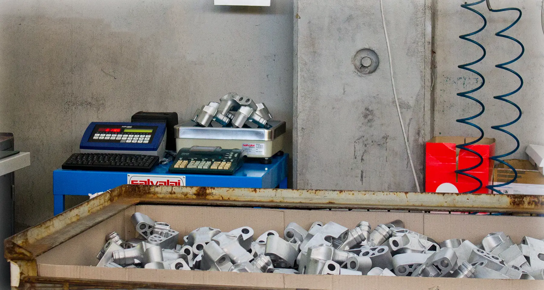 Postazione di pesatura con bilancia contapezzi e indicatore di peso Salvalai, davanti a un cassone di pezzi metallici